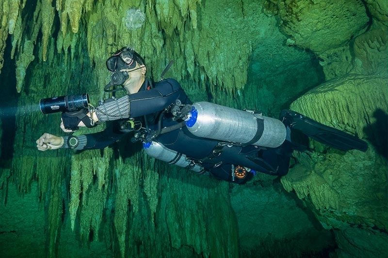 Scuba diver maintaining horizontal trim inside a green underwater cave