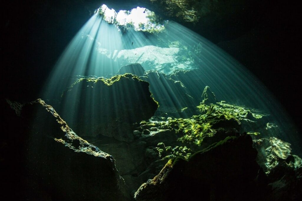 Sunbeams illuminate moss-covered rocks inside a submerged cave