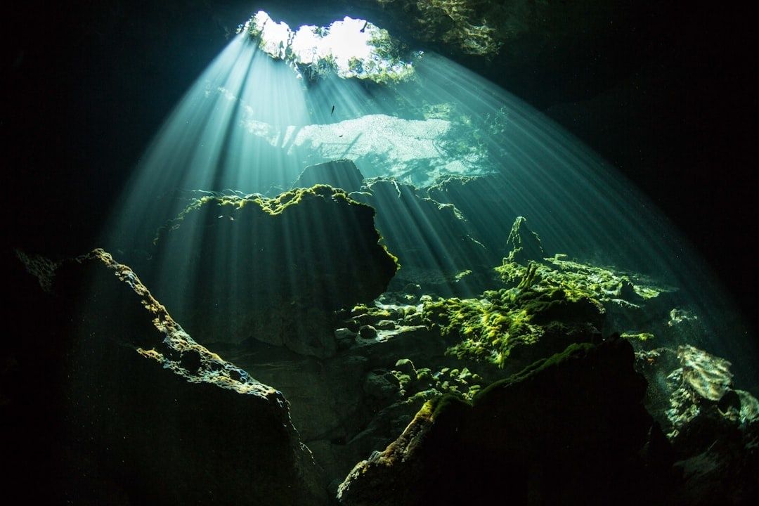 Sunbeams illuminate moss-covered rocks inside a submerged cave